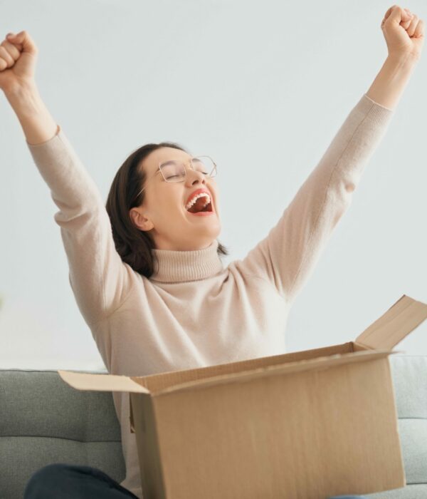 Jeune femme heureuse avec un carton de livraison ouvert sur ses jambes assise en tailleur sur son canapé à la maison.